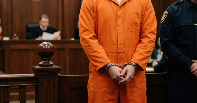 media-vecteezy_a-man-in-an-orange-jumpsuit-stands-in-front-of-a-judge_78720861